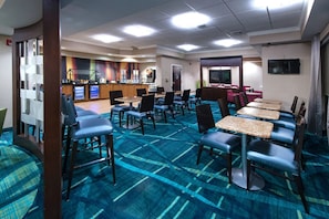 A hotel dining area with tables and chairs, a kitchen in the background, and a TV on the wall. - Stretch Out and Settle In Near Greensboro Hotspots l Heated Pool & Breakfast (Greensboro)
