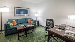 A hotel room with a teal sofa, a coffee table, a desk with a laptop, a telephone, and a framed abstract painting on the wall. - Stretch Out and Settle In Near Greensboro Hotspots l Heated Pool & Breakfast (Greensboro)