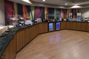 A breakfast bar with a variety of food items, a coffee machine, and a refrigerator.