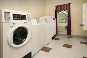 A laundry room with a front-loading washer and dryer, a window with a curtain, and a radiator.