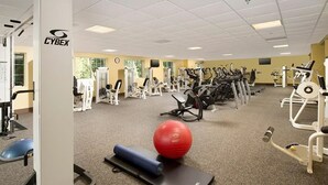 Ein Fitnessstudio mit unterschiedlichen Trainingsgeräten, einem roten Trainingsball und einer schwarzen Yogamatte.