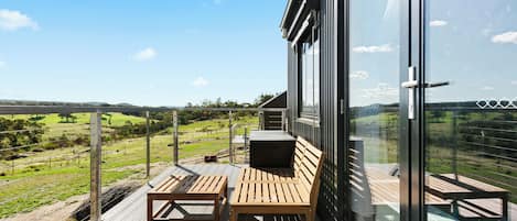 A wooden deck with a bench and table, overlooking a green landscape.