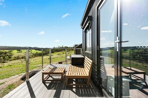 A wooden deck with a bench and table, overlooking a green landscape.