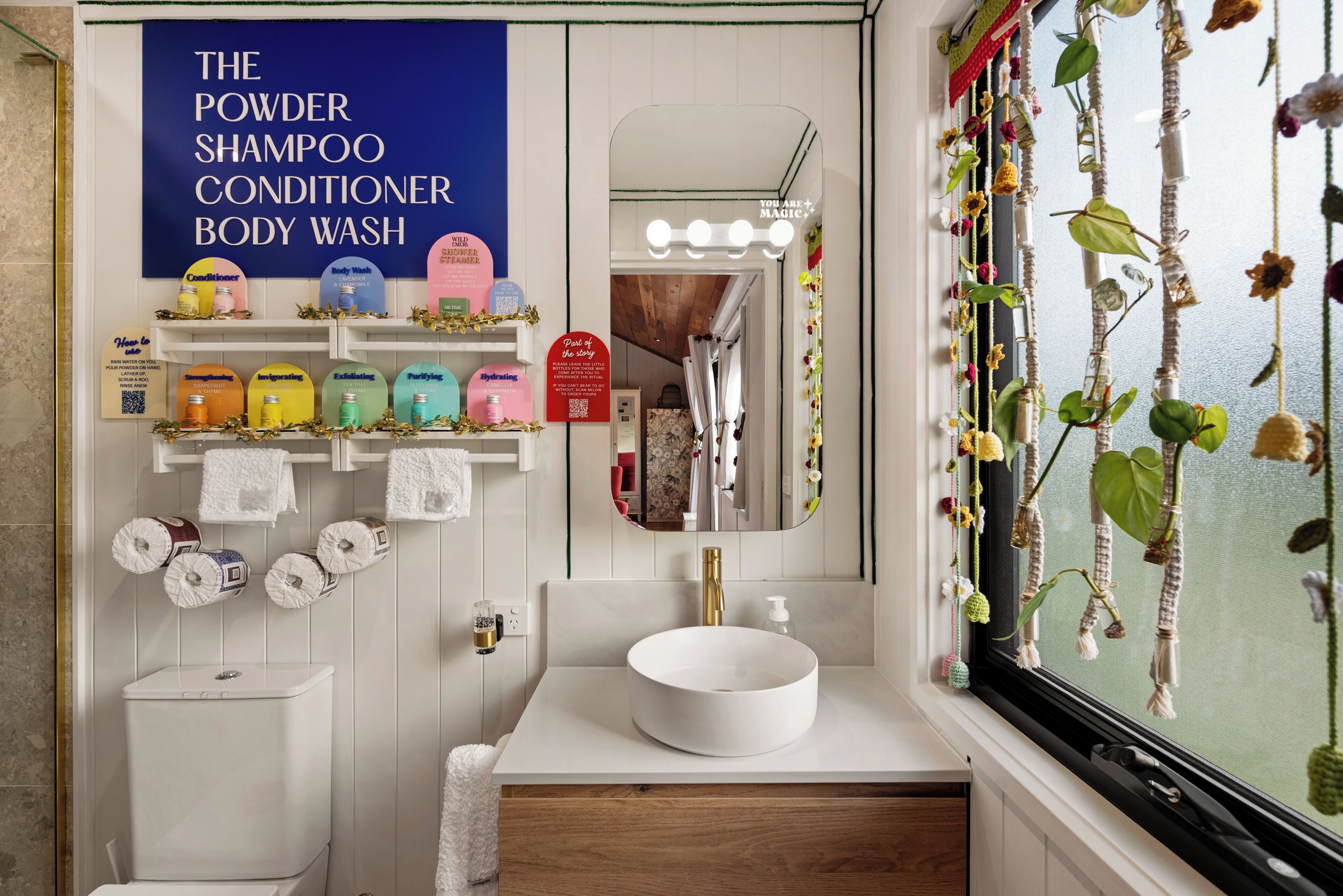 Un baño con tocador, un espejo grande y una ventana con vistas a plantas.