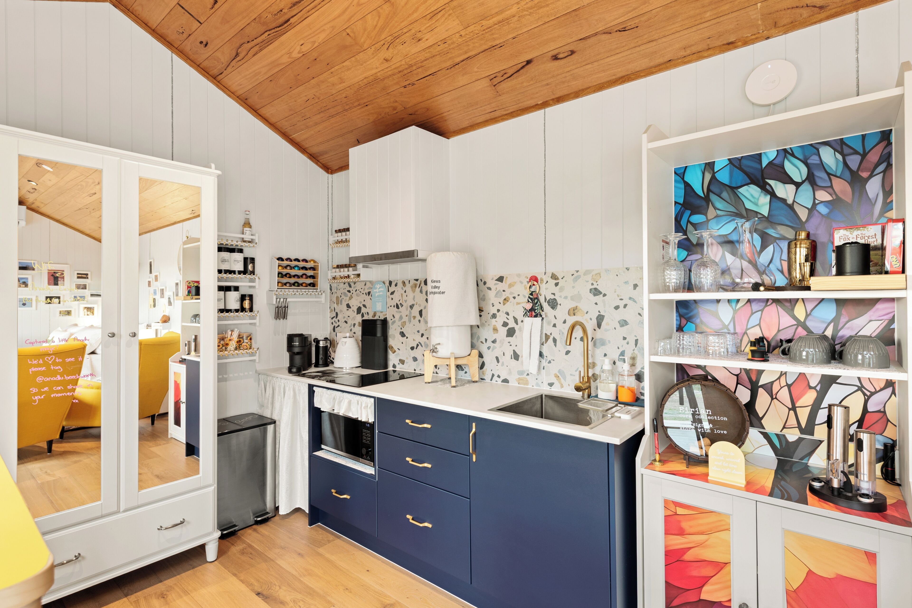 A modern kitchen with white cabinetry, a wooden ceiling, and a colorful abstract wall art piece.