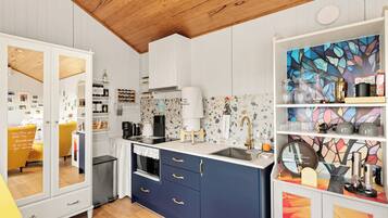 A modern kitchen with white cabinetry, a wooden ceiling, and a colorful abstract wall art piece.