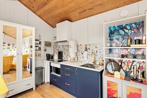 Una cocina moderna con armarios blancos, techo de madera y una llamativa obra de arte abstracta en la pared.