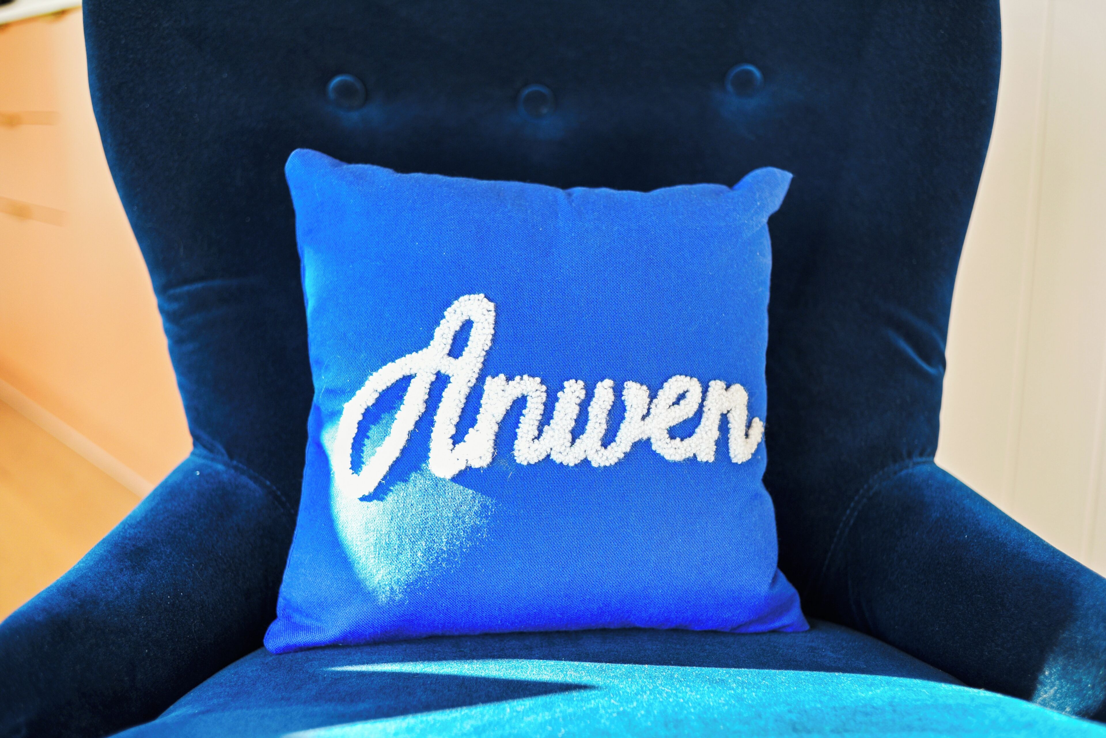 A chair with a blue cushion featuring embroidered text.