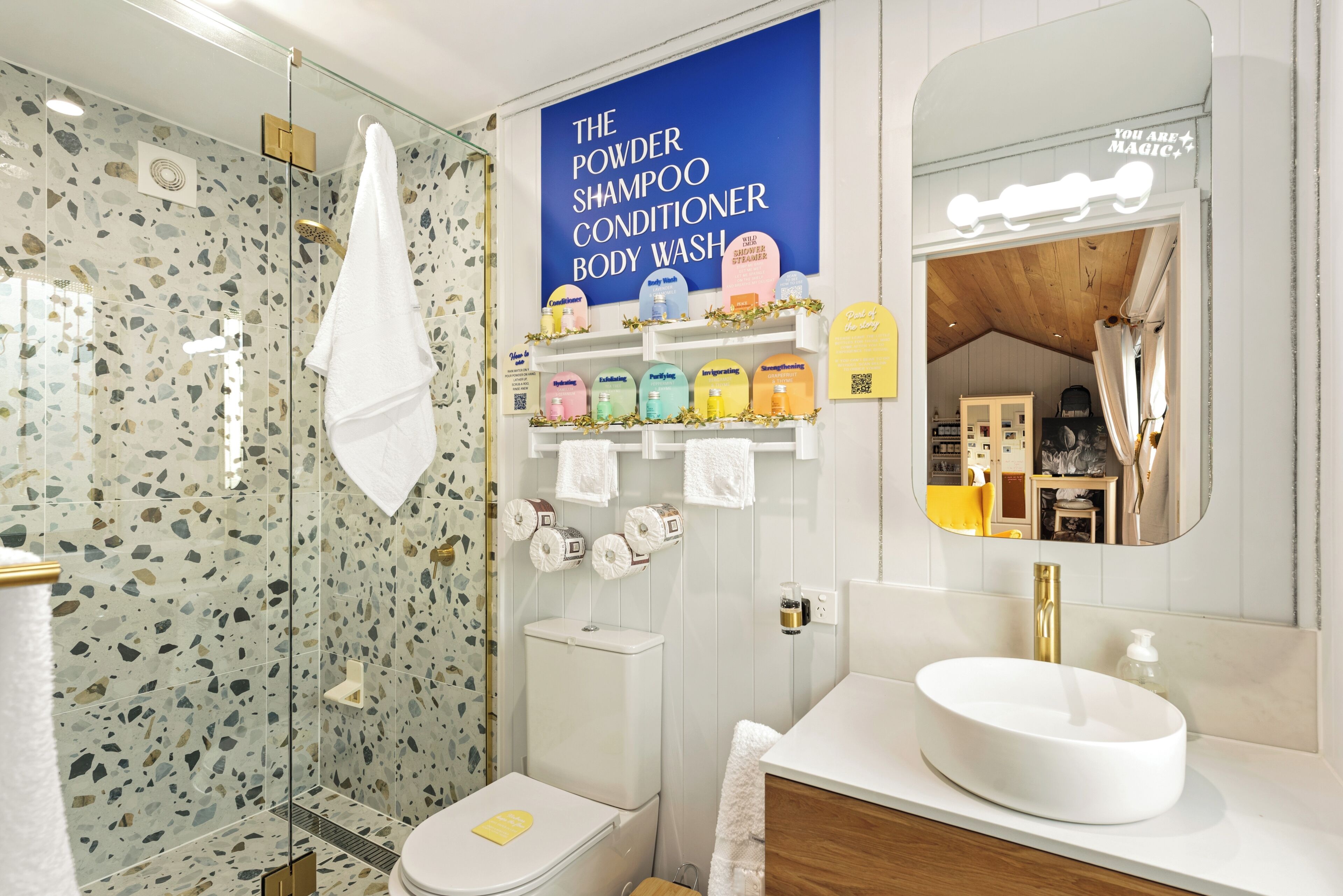 Un baño moderno con ducha, inodoro y tocador. Hay un cartel que anuncia jabón de baño y champú.