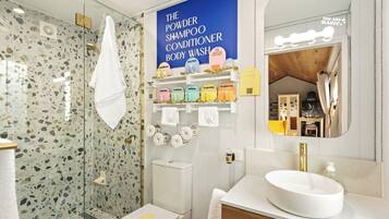 Un baño moderno con ducha, inodoro y tocador. Hay un cartel que anuncia jabón de baño y champú.