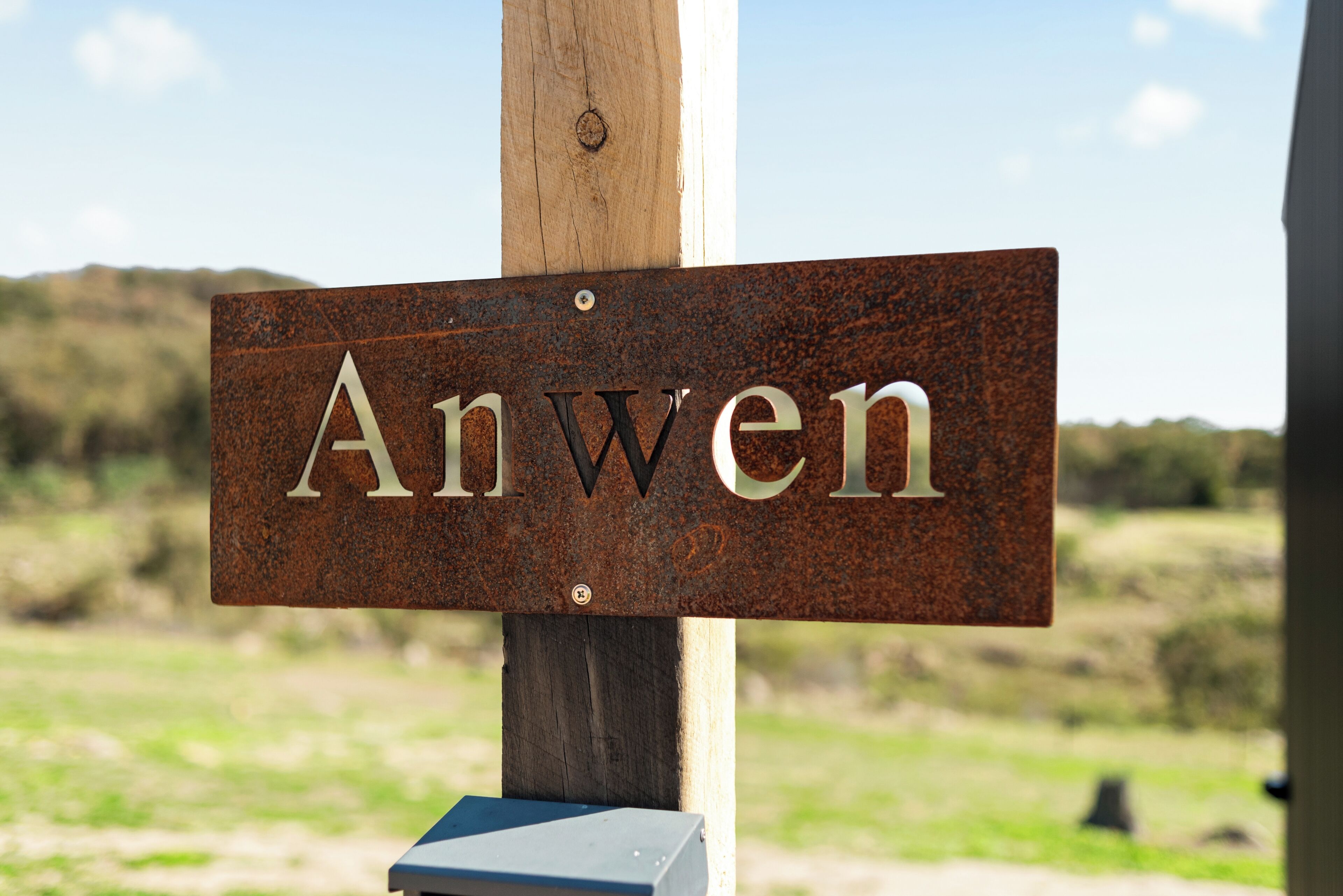 A metal sign with the word 'Anwen' mounted on a wooden post.
