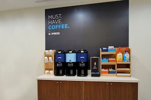 Eine Kaffeestation mit mehreren Kaffeeautomaten, einer Warmwasserstation und verschiedenen Kaffeesorten auf Regalen.