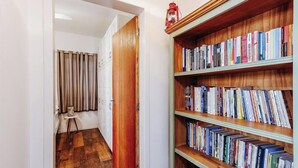Un pasillo con una estantería de madera llena de libros, una mesita con una lámpara y una puerta que da a otra habitación.