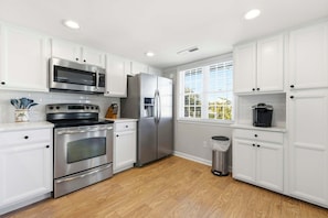 A modern kitchen with white cabinetry, stainless steel appliances, and a window providing natural light. - Pal's Palmetto Place - 3BR Bungalow w/ Ocean Views (North Myrtle Beach)