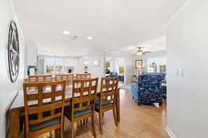 A dining area with a wooden table and chairs, a blue patterned sofa, and a ceiling fan. - Pal's Palmetto Place - 3BR Bungalow w/ Ocean Views (North Myrtle Beach)