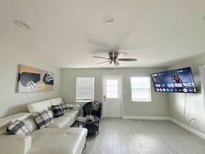 A living room with a white sofa, a ceiling fan, a flat-screen TV, and a door. - Home close to Clearwater beach (Largo)