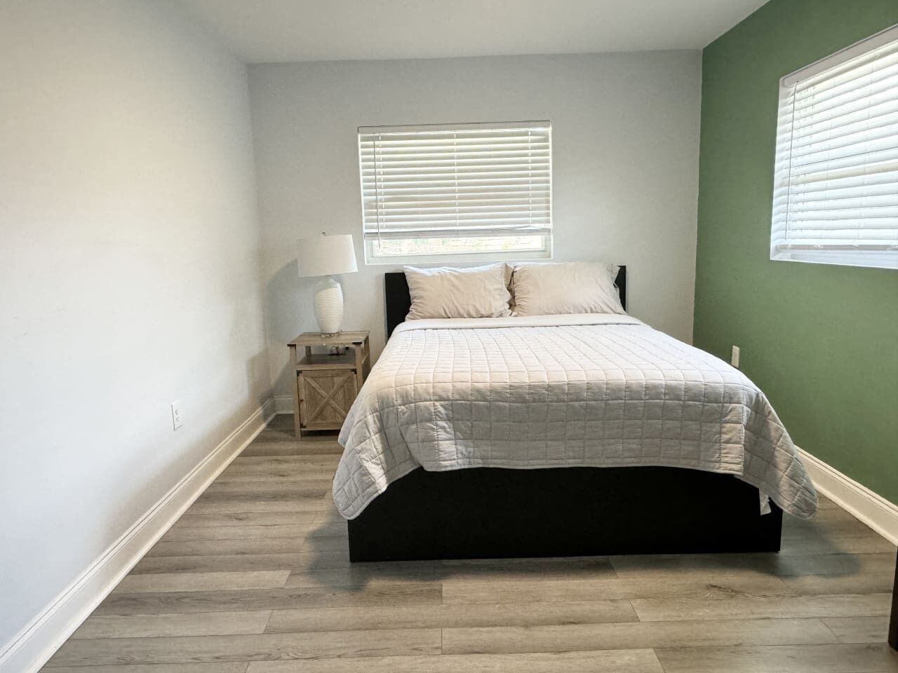 A bedroom with a bed, a nightstand, a lamp, and a window with blinds.