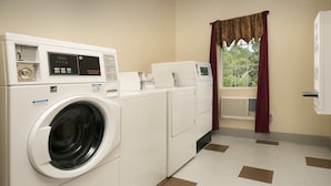 Uma lavanderia com máquina de lavar e secar de abertura frontal, uma janela com cortinas e um radiador.