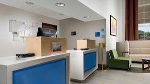 A hotel reception area with a modern design, featuring a reception desk, a green sofa, and a large window offering a view of the outdoors. - Wake Up to Free Breakfast Before Your Virginia Adventure (Ruckersville)