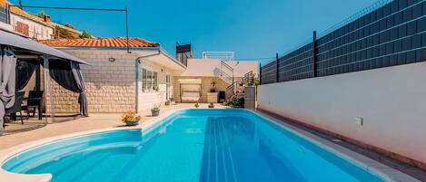A swimming pool with a clear blue water, surrounded by a white wall and a fence.
