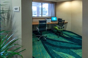 Una sala de biblioteca para negocios con dos escritorios, sillas, una impresora y un ventanal con vistas a edificios.