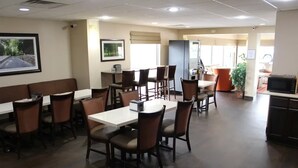 A restaurant with a long white table and multiple chairs, a counter with a cash register, and a refrigerator. - Affordable Stay Near Liberty University with Free Breakfast & Outdoor Pool (Lynchburg)