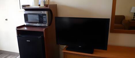 A hotel room with a microwave, a television on a wooden dresser, and a trash bin.