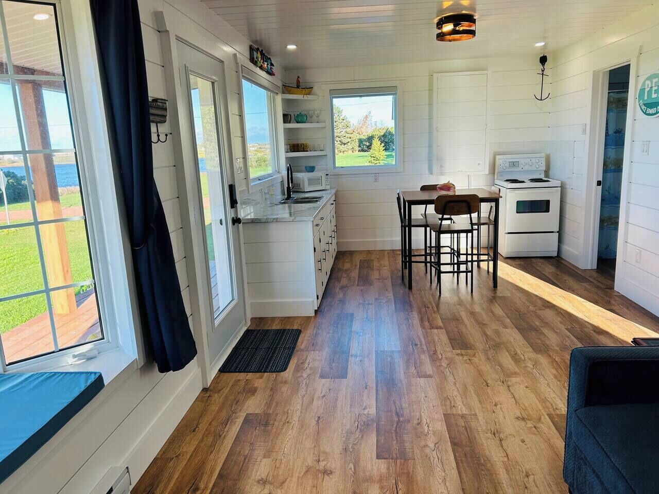 A compact kitchen with a dining area, wooden flooring, and large windows offering a view.