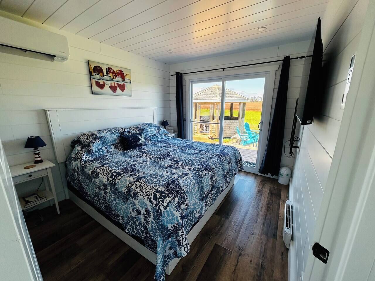 Une chambre à coucher comprenant un lit, une table de chevet, une lampe, une fenêtre et une porte donnant sur un espace extérieur.