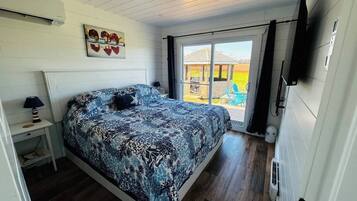 Une chambre à coucher comprenant un lit, une table de chevet, une lampe, une fenêtre et une porte donnant sur un espace extérieur.