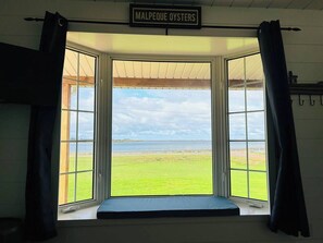 A room with a large window overlooking a grassy area and a body of water, with a sign above reading 'MALPEQUE OYSTERS'.