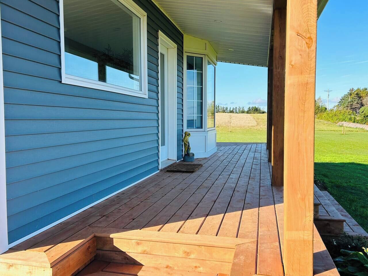 Une terrasse en bois menant à une maison aux murs recouverts de bardage bleu et aux ornements blancs.