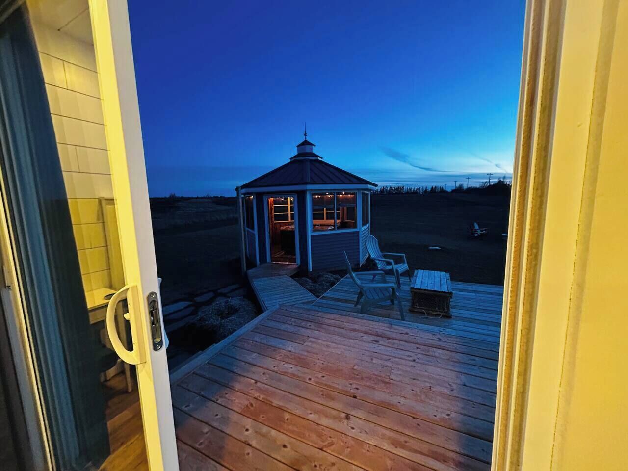 Una terraza de madera con un mirador, sillas, una puerta y una vista de un edificio al fondo.