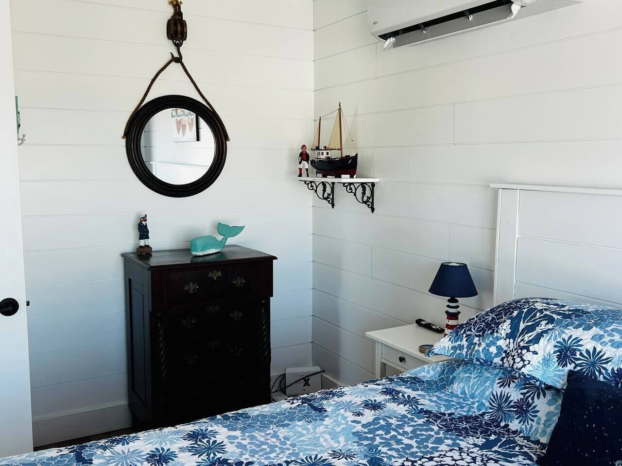 Quarto com cama, cômoda, espelho, luminária e estante com modelo de navio.
