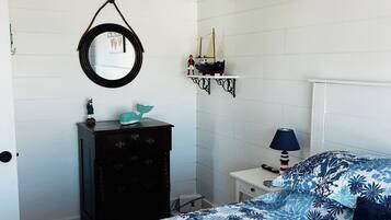 Quarto com cama, cômoda, espelho, luminária e estante com modelo de navio.