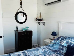 Un dormitorio con cama, cómoda, espejo, lámpara y una estantería con un modelo de barco.