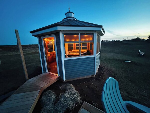 A small, light blue wooden structure with a porch and a door leading inside.