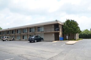 A multi-story motel with a parking lot, a trash bin, and a tree in front.