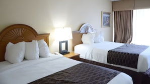 Habitación de hotel con dos camas, una mesita de noche con lámpara, cabecero y un cuadro en la pared.