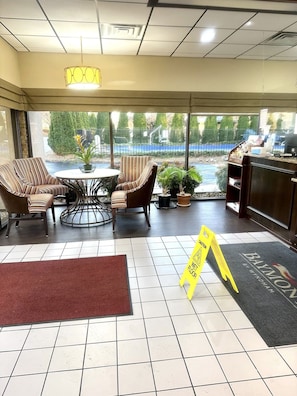 A hotel lobby with a wet floor sign, a reception desk, and a seating area with striped chairs and a small table.