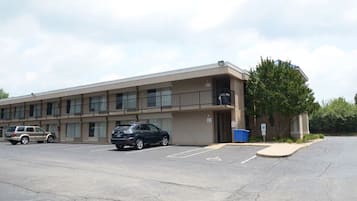A multi-story motel with a parking lot, a trash bin, and a tree in front.