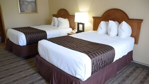 To dobbeltsenge med brune sengegavl og hvidt sengetøj på et hotelværelse.