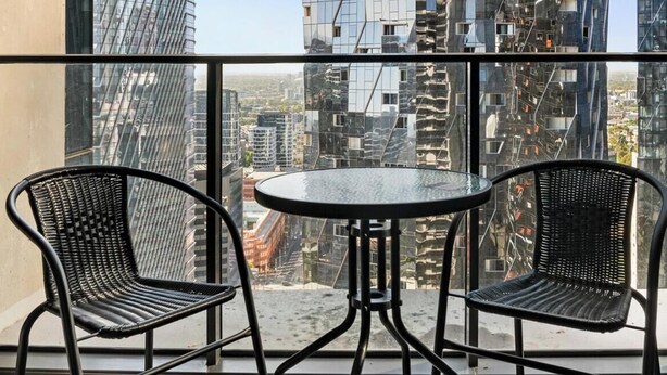 Un balcón con dos sillas y una mesa, con vista a un paisaje urbano con edificios modernos.