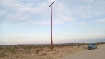 A desert landscape with sparse vegetation, a single utility pole, and a parked car on a dirt road.