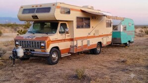 Una caravana vintage con un techo grande extendido, un remolque más pequeño acoplado y un tanque de gas montado en la parte delantera.