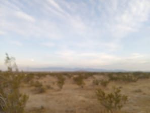 A desert landscape with sparse vegetation and distant mountains under a partly cloudy sky.