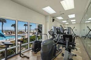 Un gimnasio con máquinas de cardio, una piscina y vistas al océano.