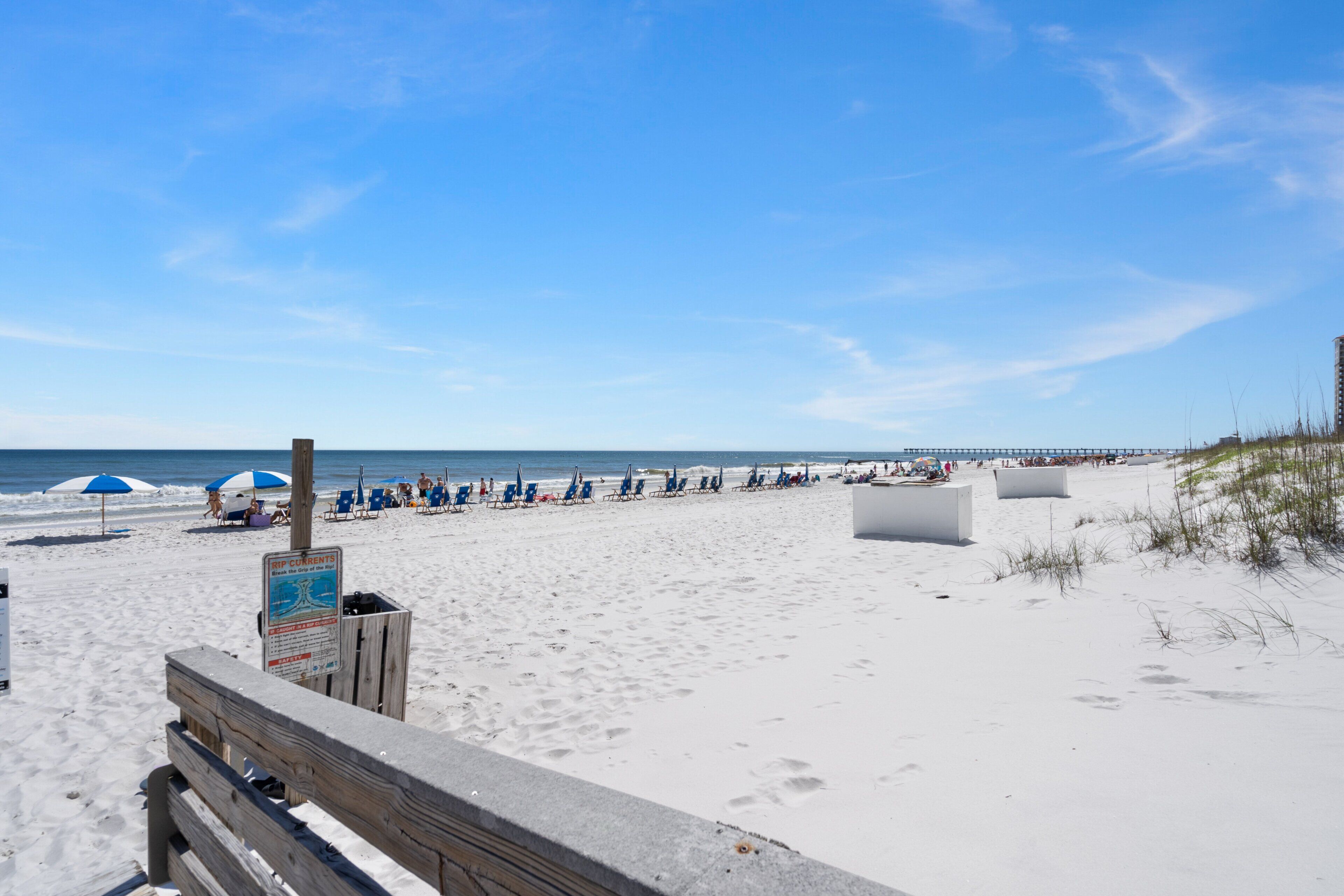 A beach with a wooden walkway, beach chairs, umbrellas, and a sign.