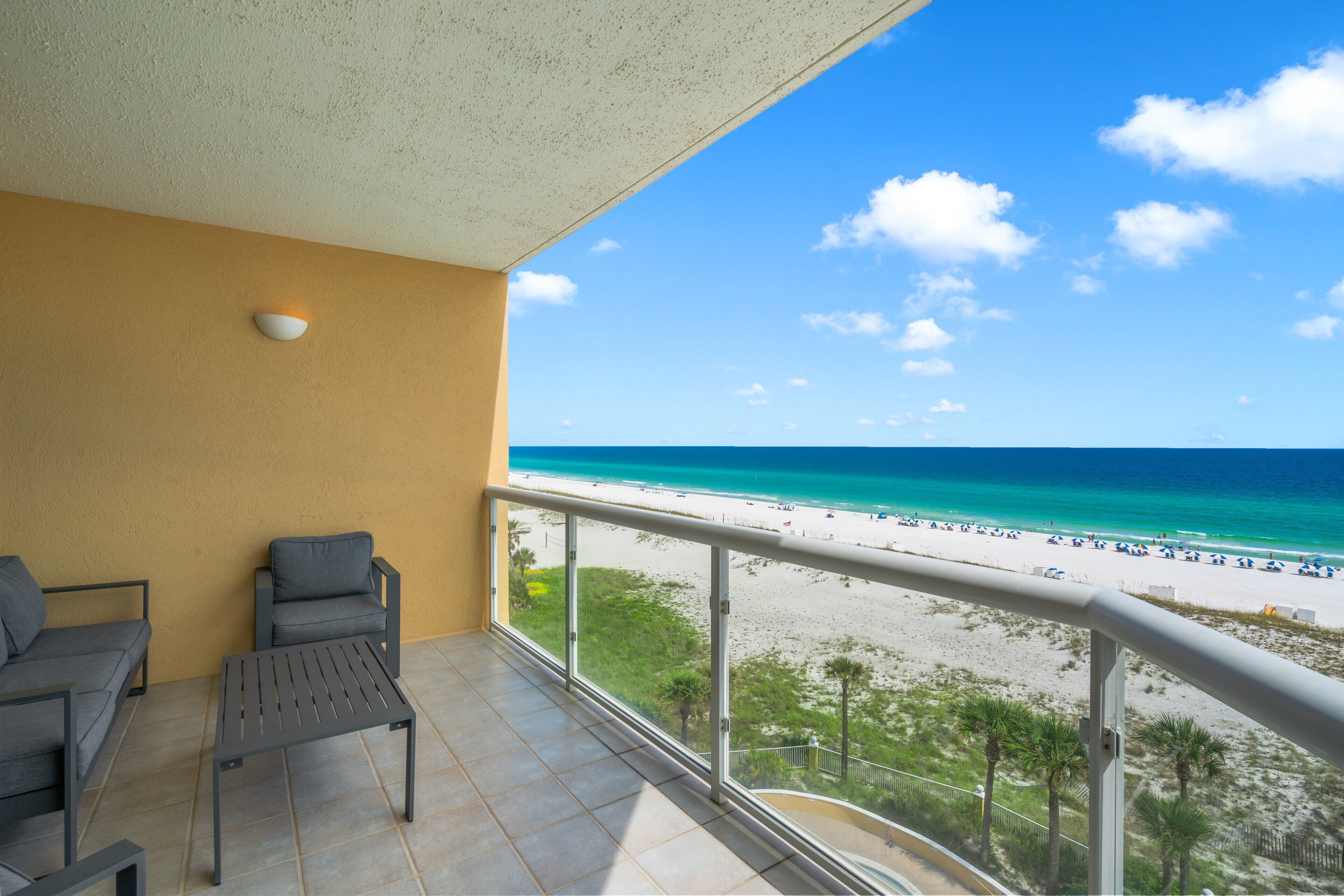 A balcony with a view of a beach, a table, and two chairs.