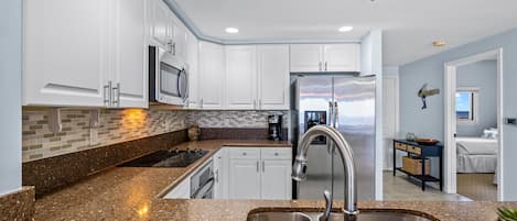 Una cocina moderna con encimeras de granito, electrodomésticos de acero inoxidable y alacenas blancas.